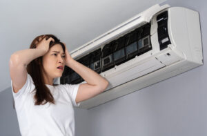 Woman looking stressed while standing near malfunctioning air conditioning unit, representing common AC issues during summer in Niagara Falls.